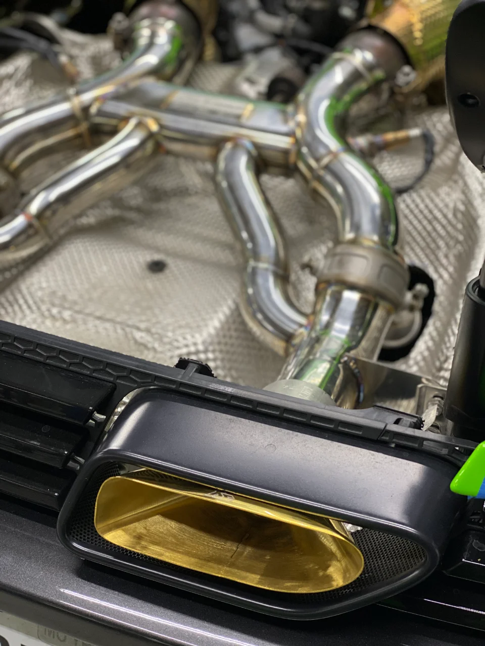 A close-up view of a custom stainless steel exhaust system with a distinctive gold exhaust tip.