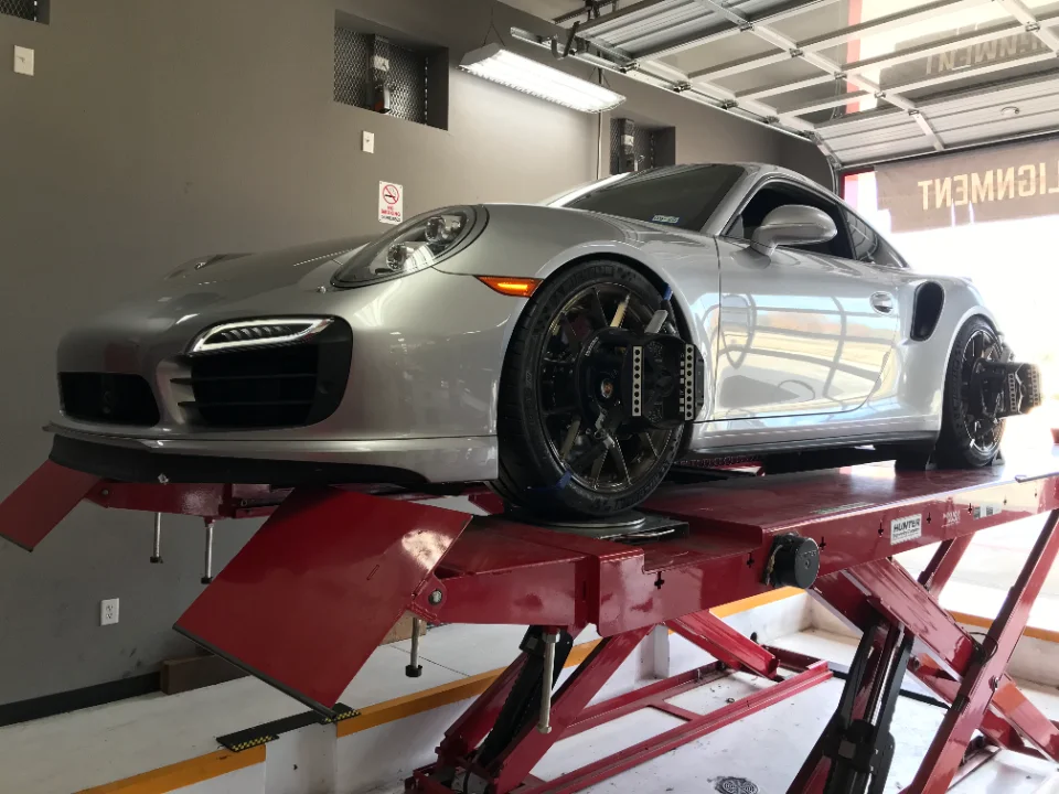 A silver Porsche 911 on a red alignment rack in a performance shop, with alignment sensors attached to its wheels.