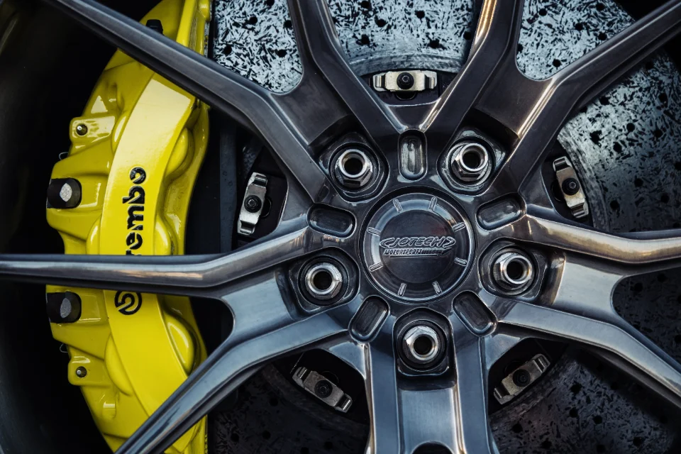 A close-up detail shot of a Jotech Motorsports car's wheel, featuring a grey multi-spoke wheel, yellow Brembo brake caliper, and a drilled rotor.