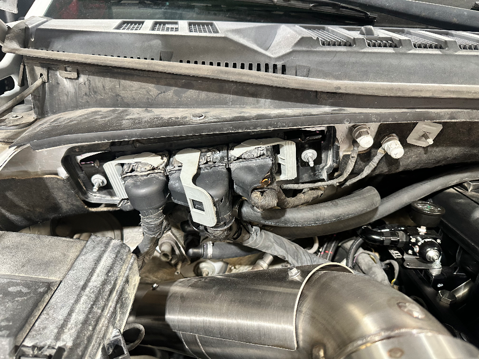 Close-up of a car's engine bay showing aftermarket fuel system components, including a fuel pressure regulator and associated lines, during a shop install.