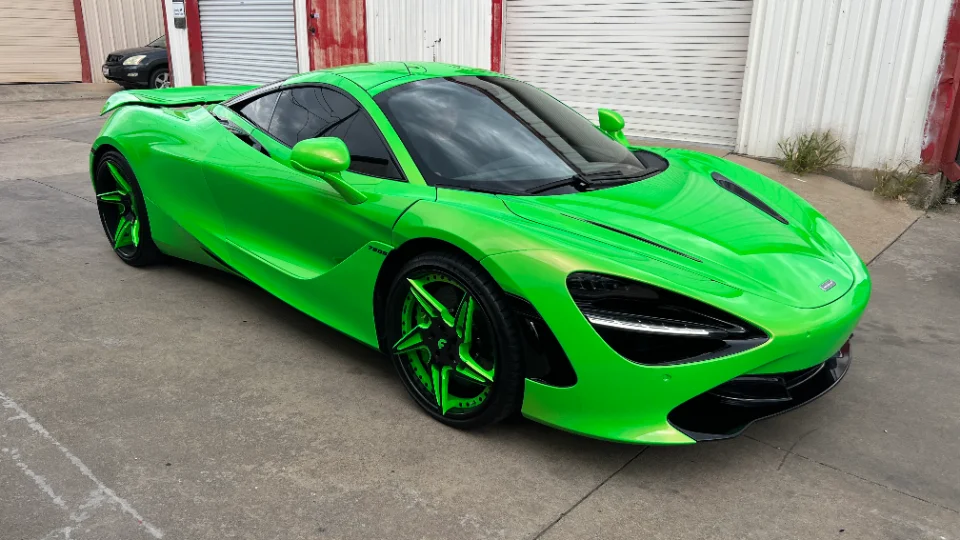 A bright green McLaren 720S supercar with custom green wheels parked on concrete in front of garage doors.