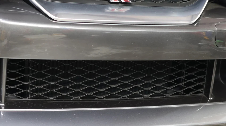 Close-up of the front bumper and lower grille of a grey Nissan GT-R, revealing an intercooler behind the mesh.