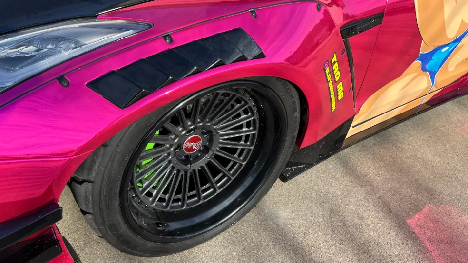 Close-up of a pink widebody Nissan GT-R with custom multi-spoke wheels and green brake calipers.