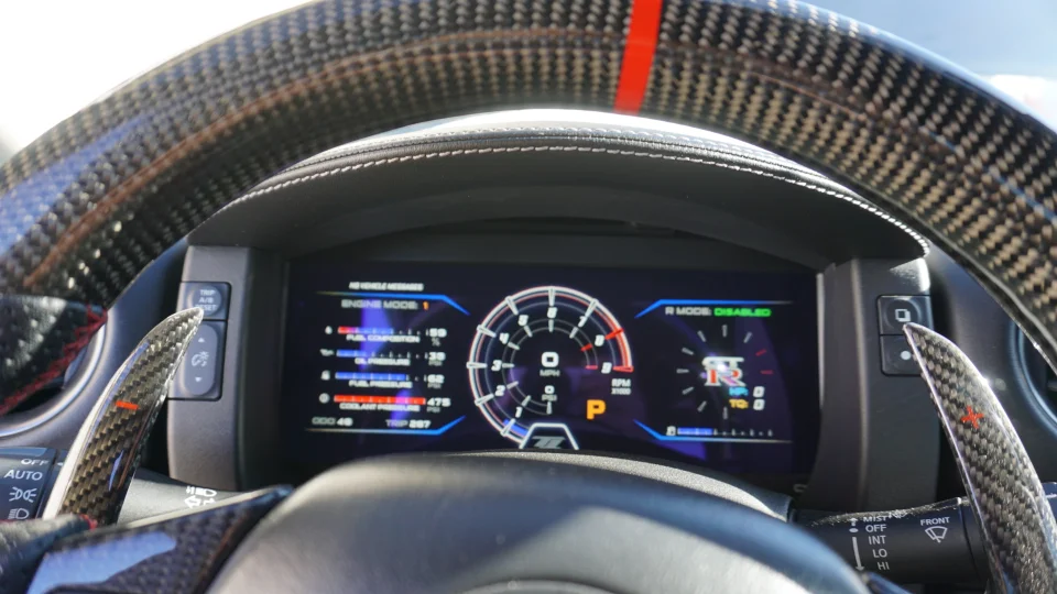 Close-up of a Nissan GT-R interior featuring a carbon fiber steering wheel, paddle shifters, and a digital performance dashboard.