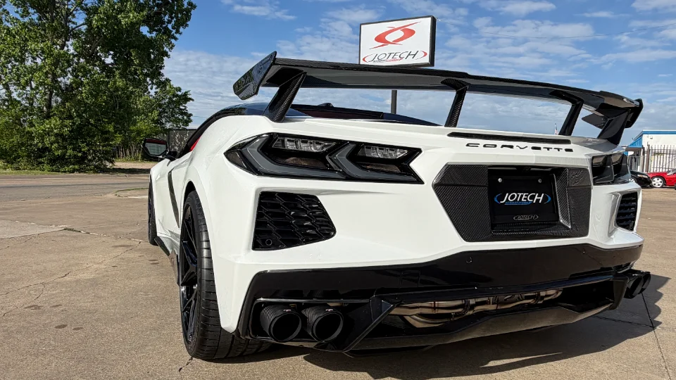 Rear view of a white C8 Corvette with a large carbon fiber wing, performance exhaust, and rear diffuser, parked outside Jotech Motorsports.