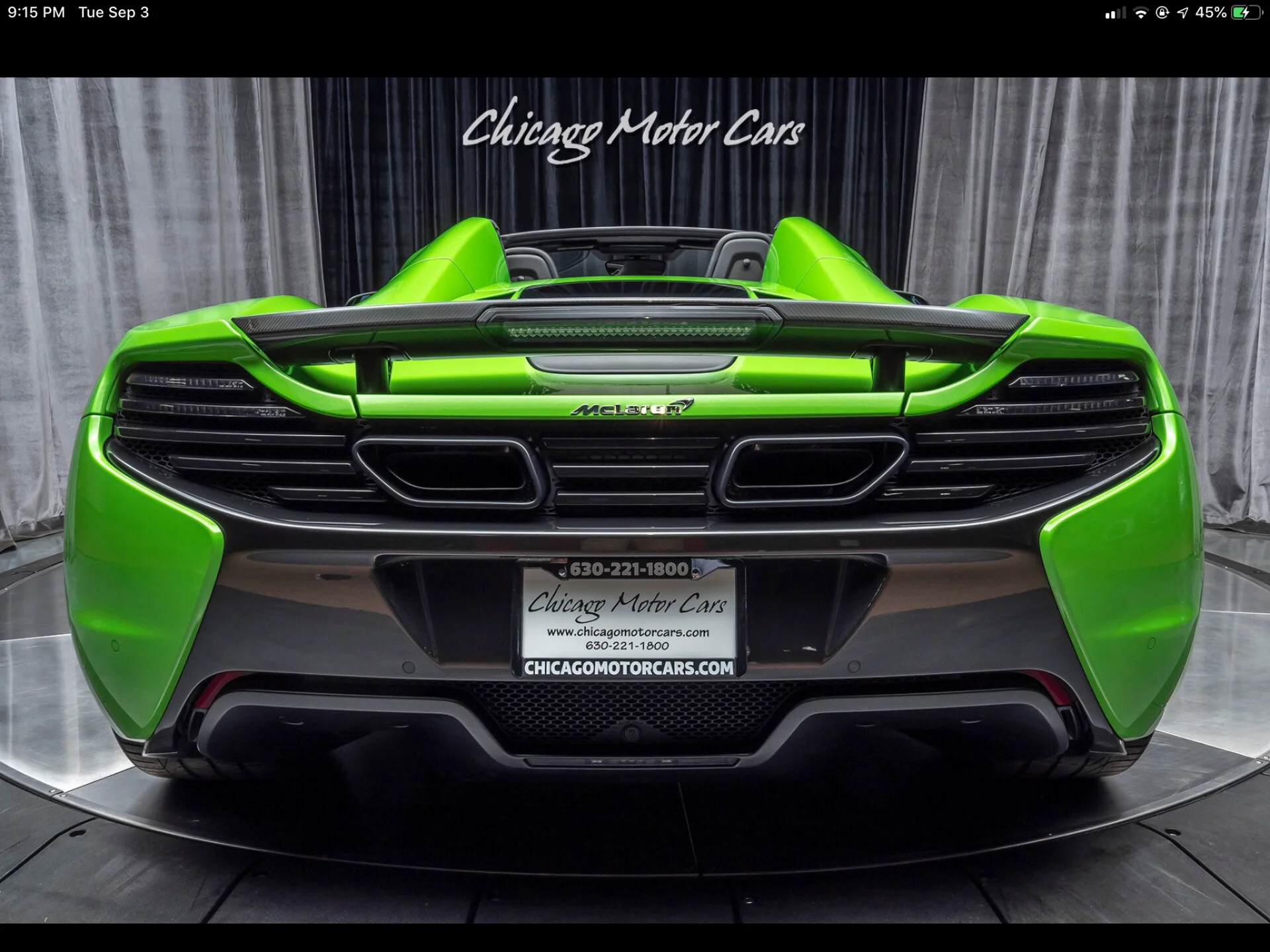 Rear view of a bright green McLaren 650S Spider with a carbon fiber spoiler in a showroom.