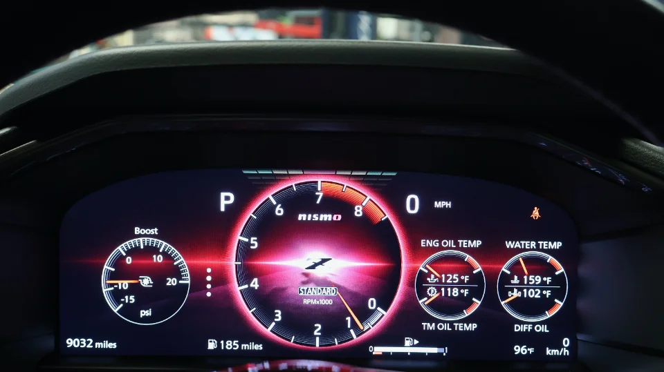Close-up of a Nissan Nismo digital dashboard displaying boost, RPM, engine oil temperature, and water temperature.