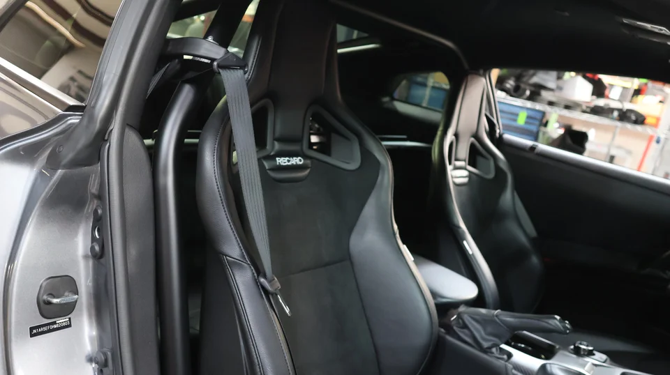 Close-up of a car's interior featuring black Recaro racing seats and a roll cage for enhanced safety.