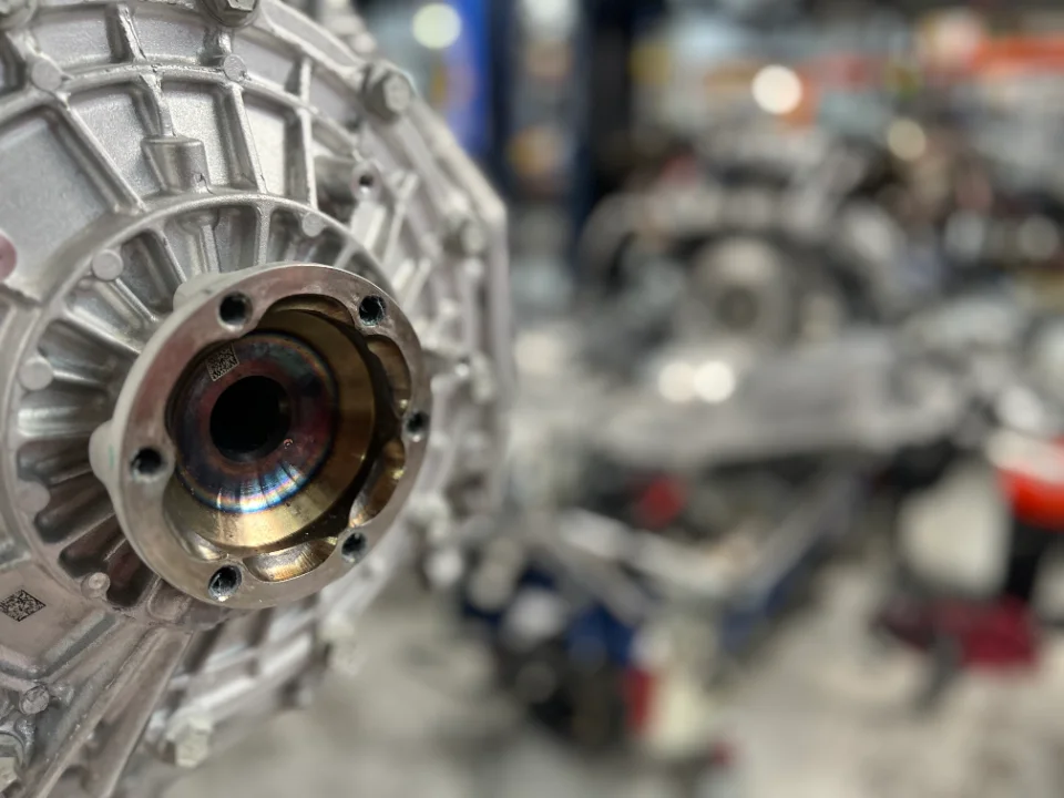 Close-up detail of a silver automotive drivetrain component, possibly a differential or transmission housing, in a workshop.