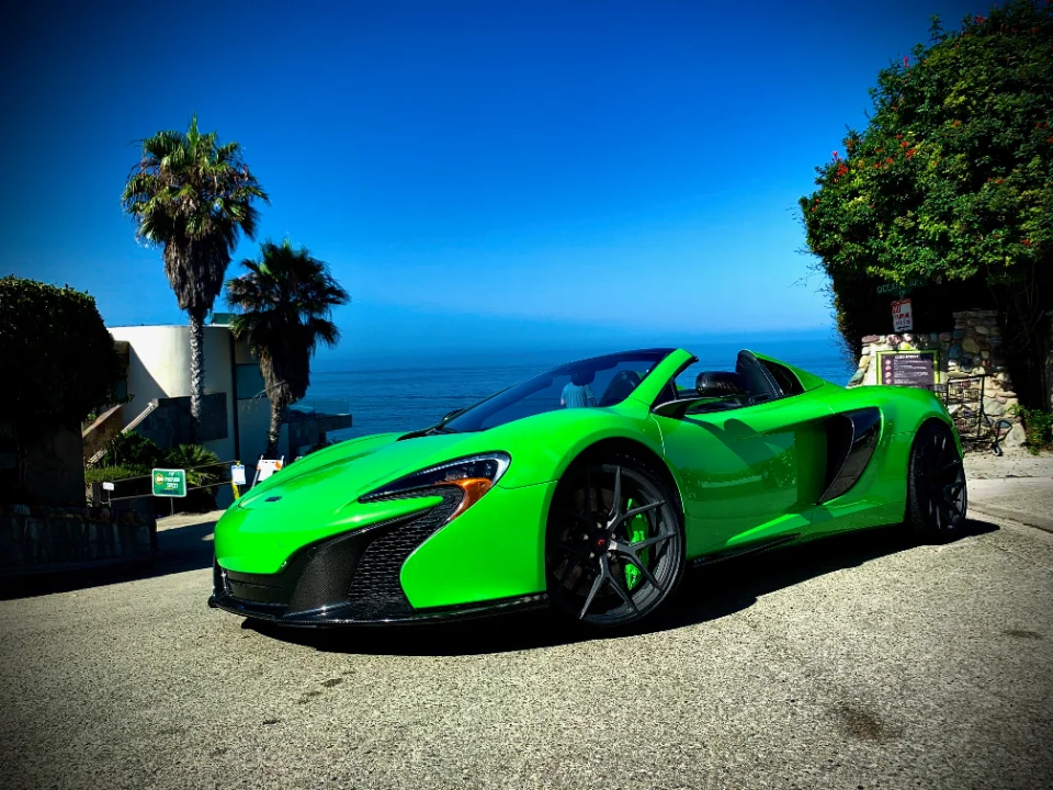 A vibrant green McLaren supercar parked on a scenic road overlooking the ocean with palm trees under a clear blue sky.