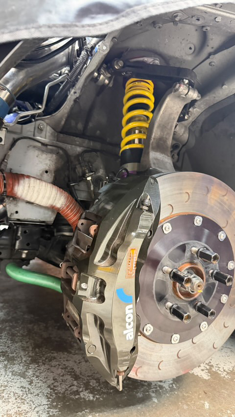 Close-up view of a performance car's front suspension with yellow coilovers and Alcon big brake kit.