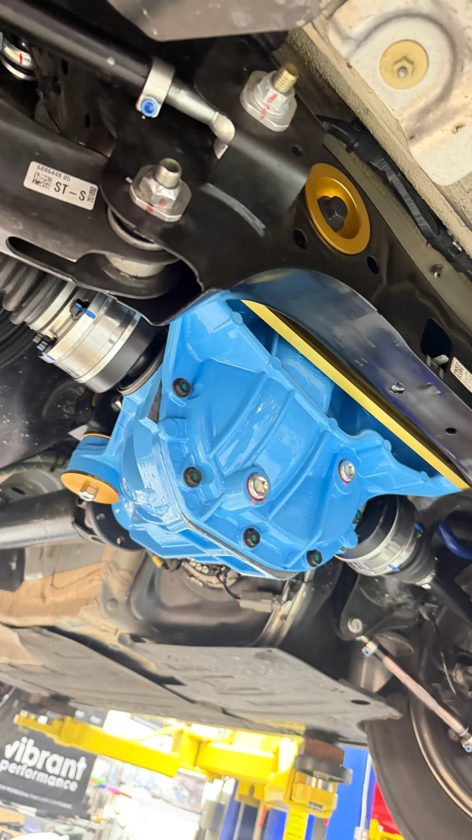 Close-up of a custom blue differential and drivetrain components installed on a car on a lift at a performance shop.