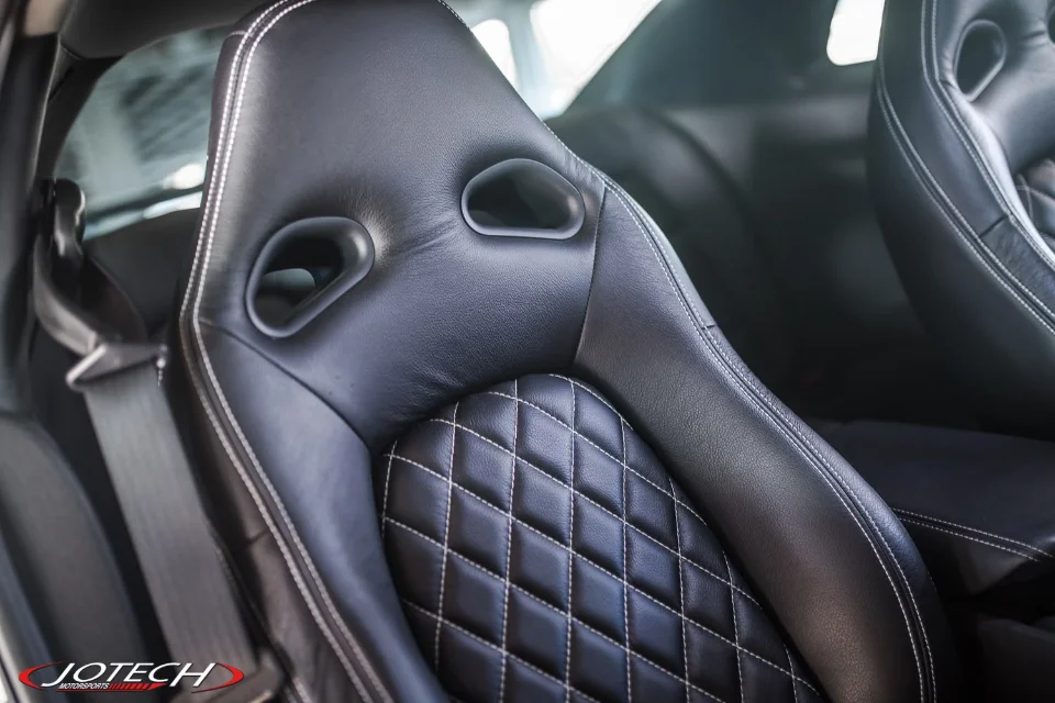 Close-up of a black leather racing seat with white diamond stitching in a performance car interior.