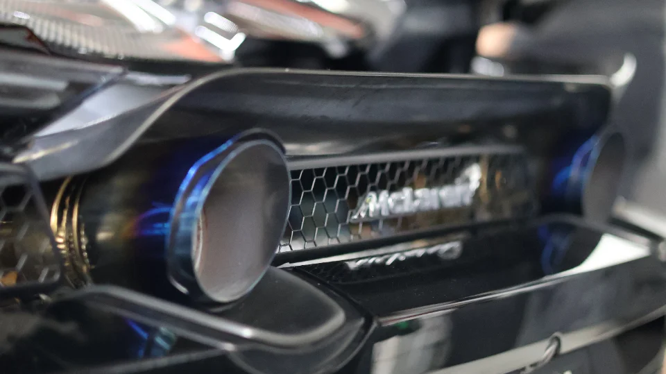 A close-up detail shot of a McLaren's rear, showcasing the blue-tinted titanium exhaust tips and honeycomb grille.