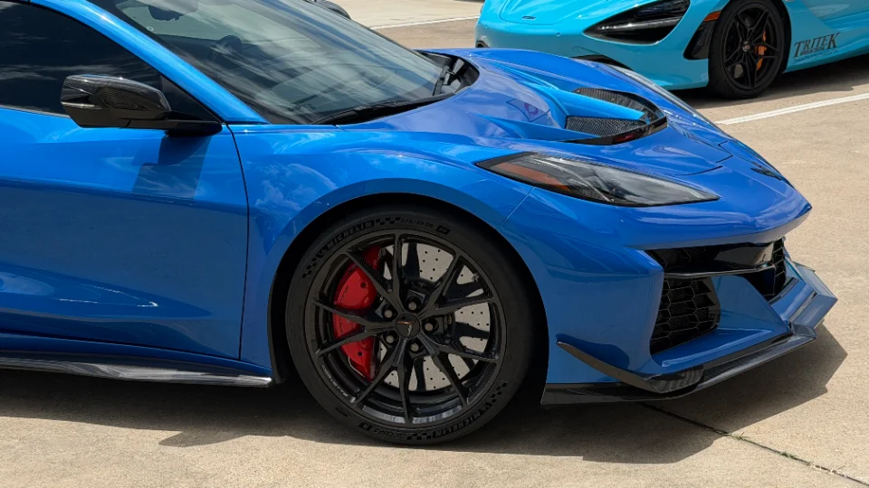 Close-up of a blue Chevrolet Corvette C8 Z06 showing its carbon fiber aero, black performance wheels, red brake calipers, and Michelin tires.