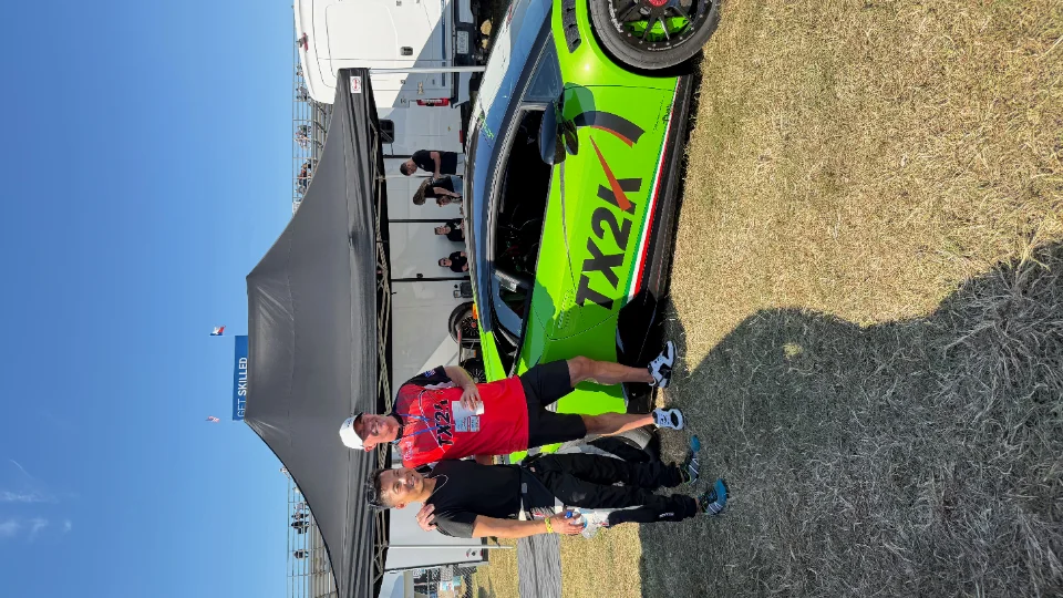 A vibrant green Lamborghini Huracan with TX2K livery is parked on grass at an outdoor event, with two men standing beside it.