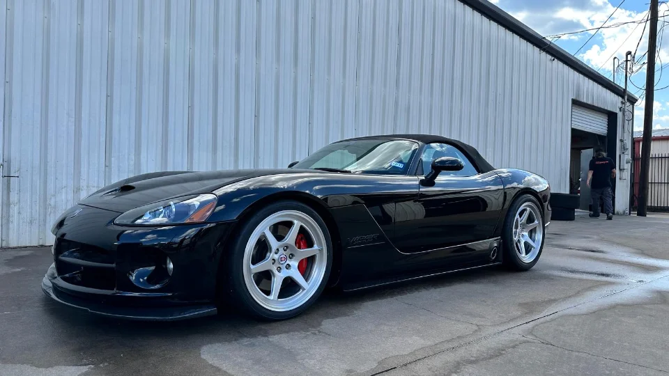 A black Dodge Viper convertible with custom silver wheels parked outside a Jotech Motorsports shop building.