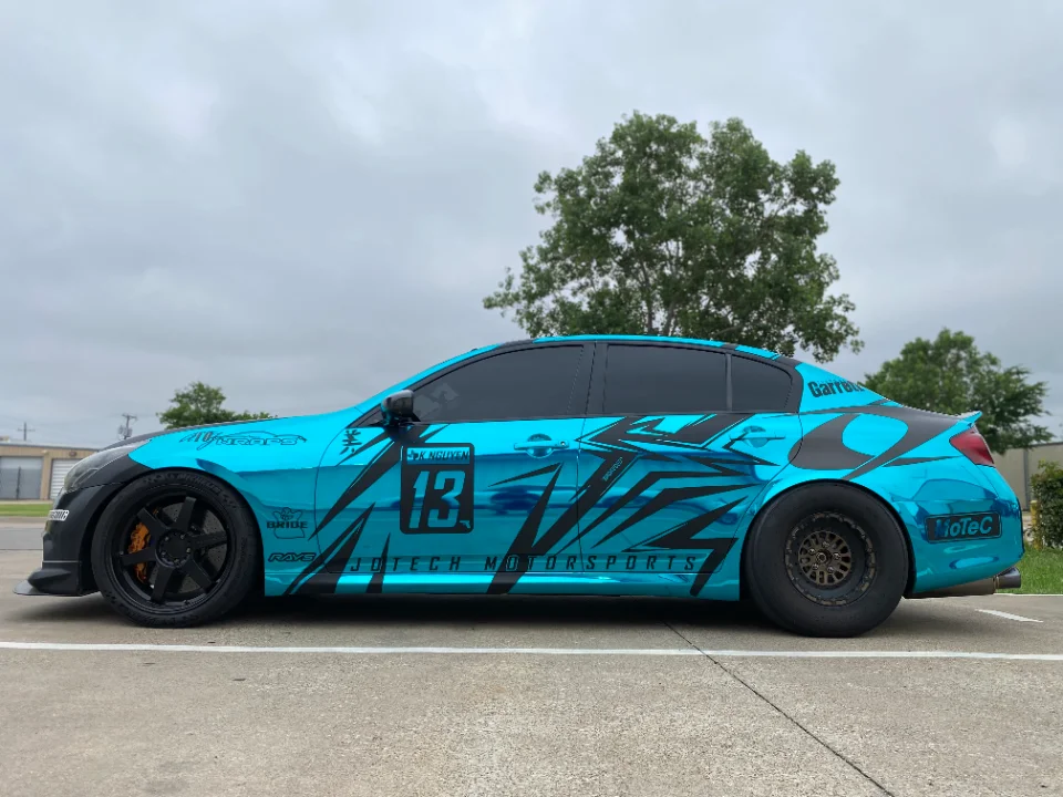 Side profile of a turquoise Infiniti G37 sedan with a custom black and blue wrap, drag wheels, and Jotech Motorsports livery.