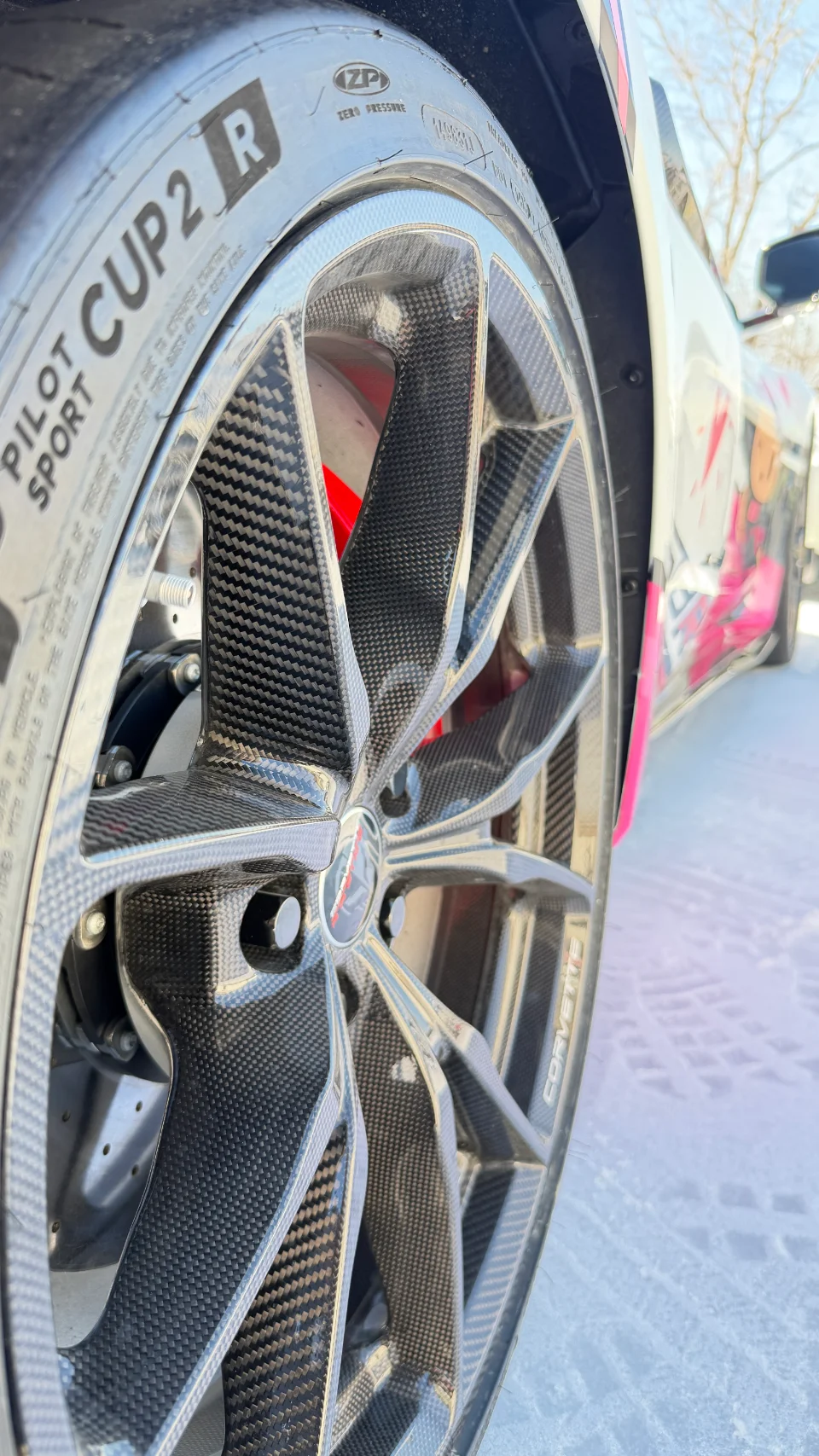 A close-up detail shot of a white Corvette's carbon fiber wheel, Michelin Pilot Sport Cup 2 tire, and red brake caliper.