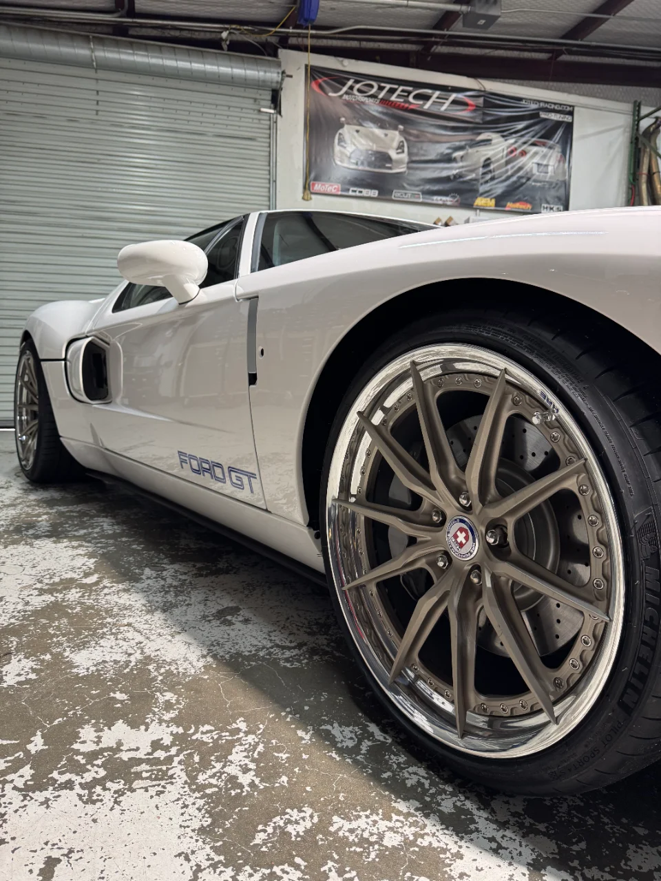 A white Ford GT with aftermarket HRE wheels and Michelin tires parked inside a Jotech Motorsports shop.