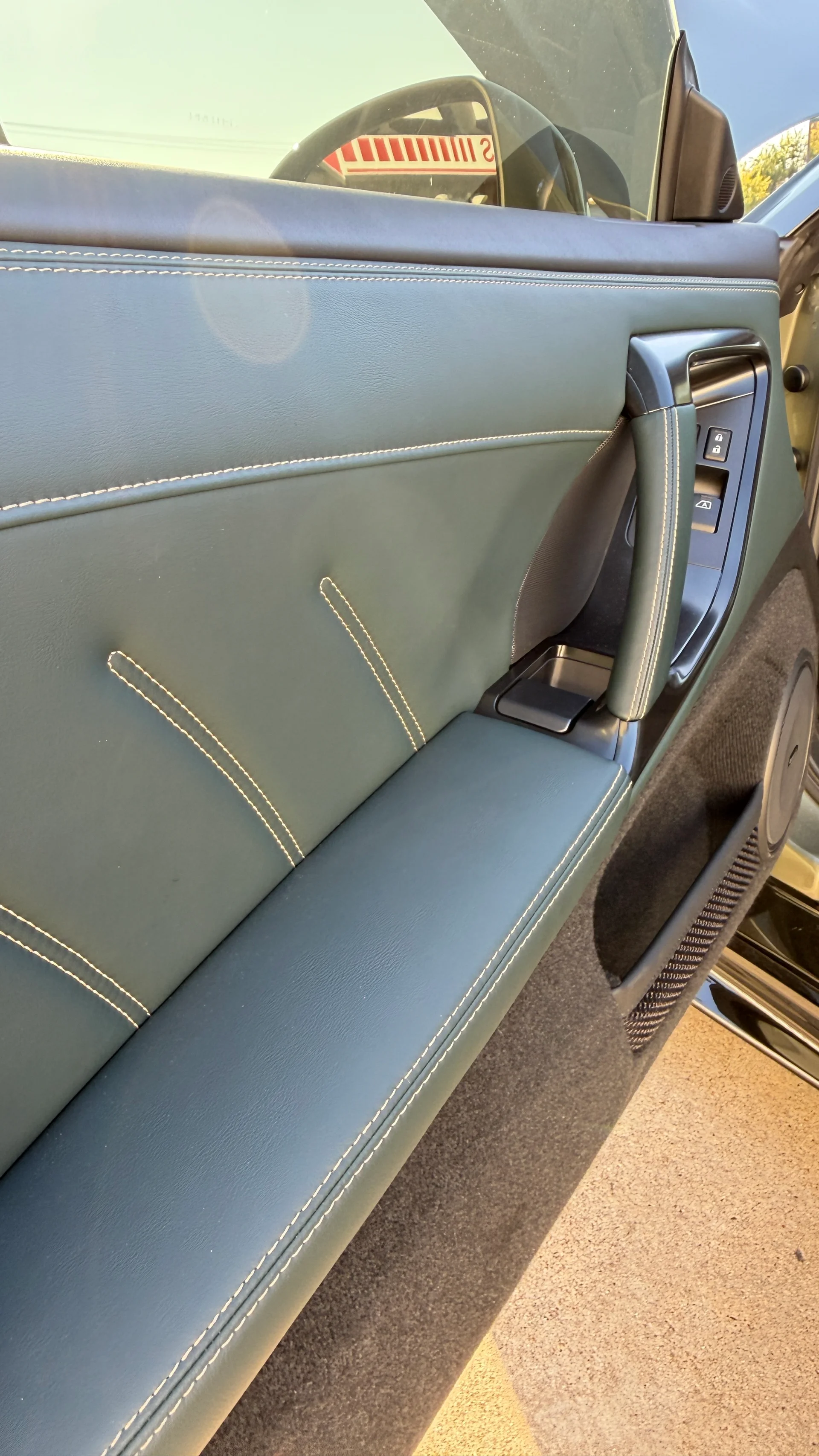 A close-up of a car's green leather interior door panel with white stitching, door handle, and window controls.