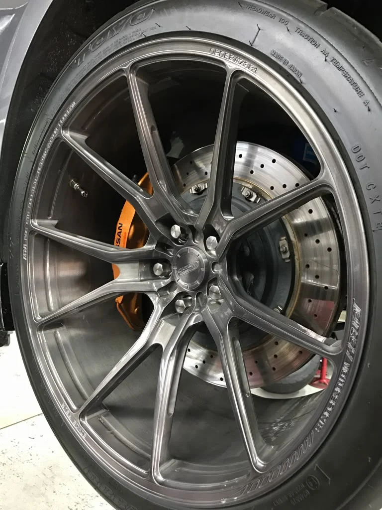A close-up of a Jotech Motorsports custom wheel with Toyo tires and Nissan orange brake calipers.