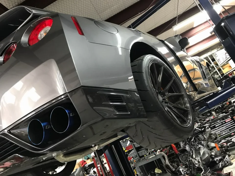Rear view of a grey Nissan GT-R on a shop lift, showcasing aftermarket exhaust tips, carbon fiber diffuser, and performance wheels.
