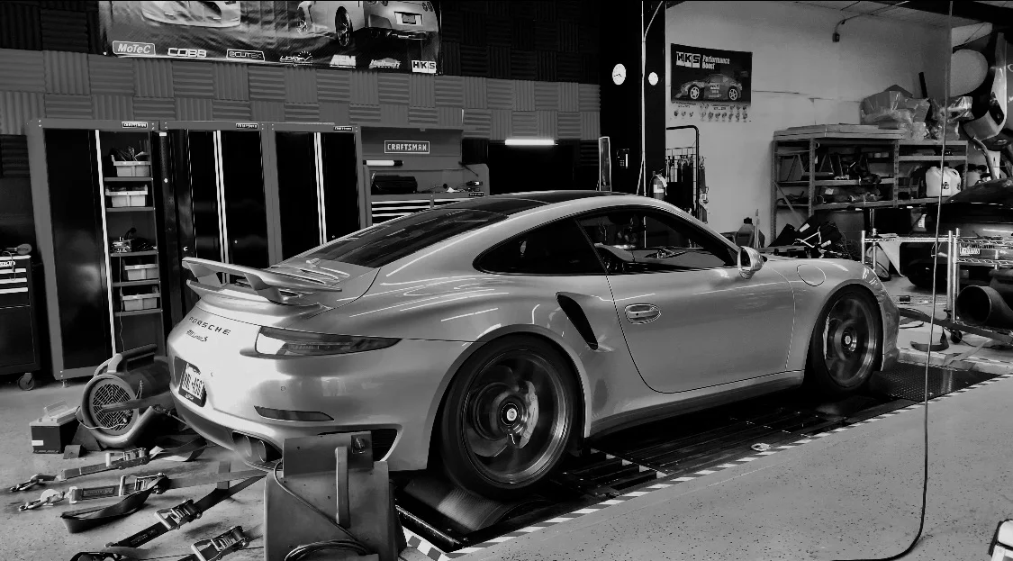 Silver Porsche 911 Turbo S on a dynamometer undergoing performance testing in a tuning shop.