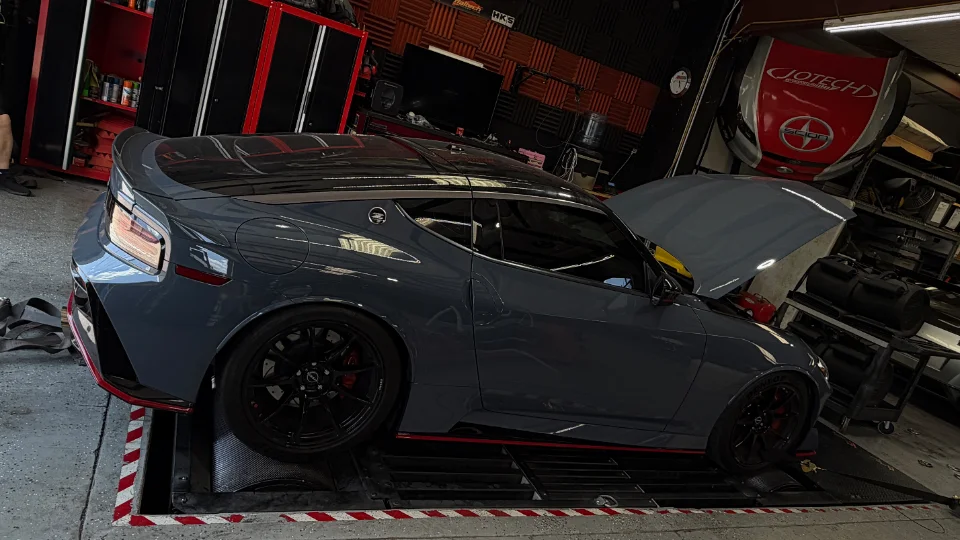 A grey Nissan Z sports car strapped to a dynamometer for performance tuning at a Jotech Motorsports shop.