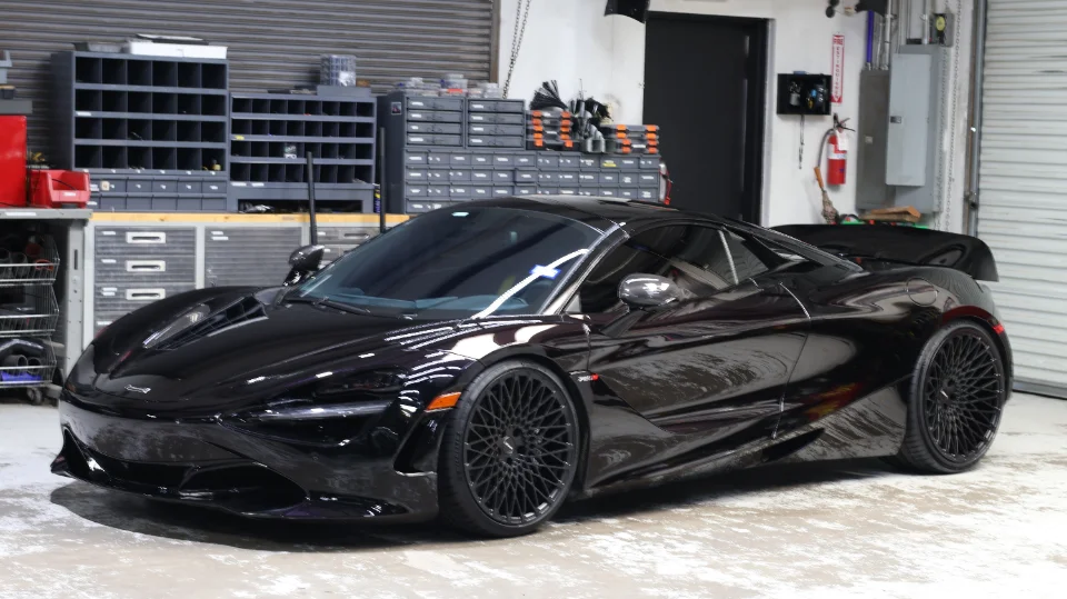 A black McLaren 720S with aftermarket wheels parked inside a performance tuning shop.