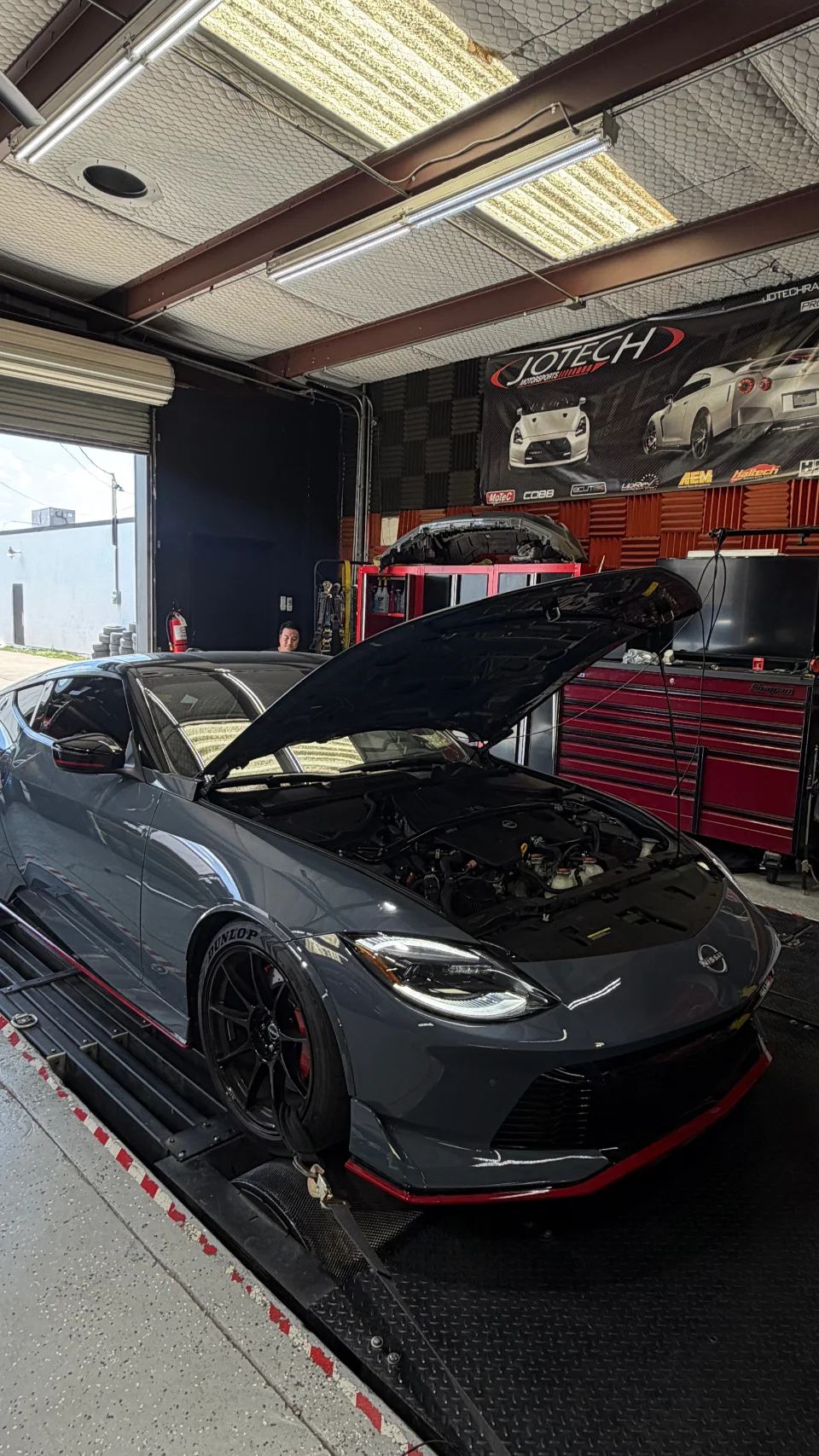 A grey Nissan Z with its hood open strapped to a dynamometer at Jotech Motorsports for performance tuning.