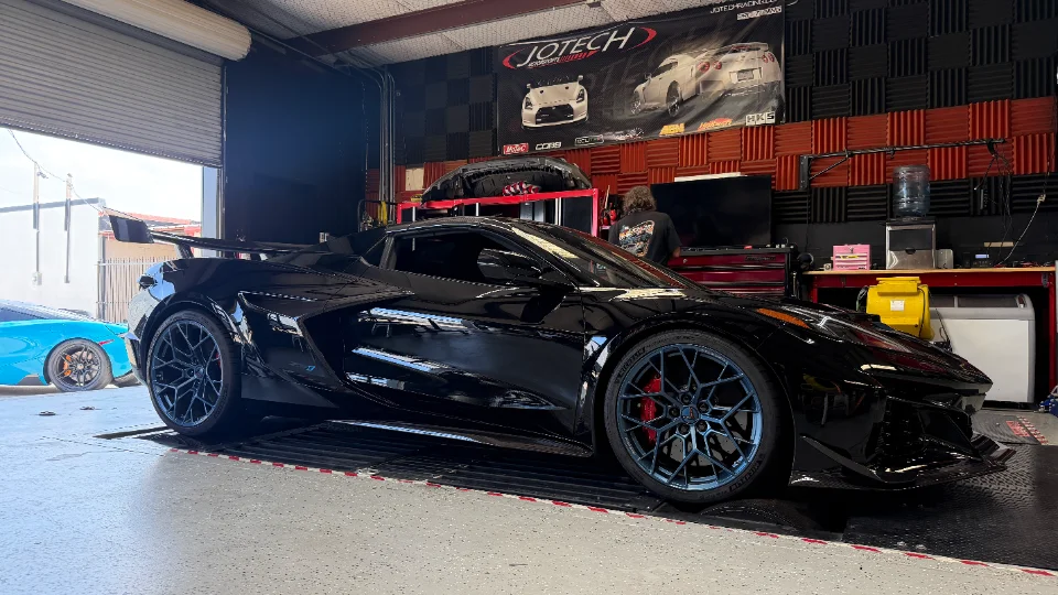 Black C8 Corvette Z06 with custom wheels and large rear wing parked inside the Jotech Motorsports performance shop.