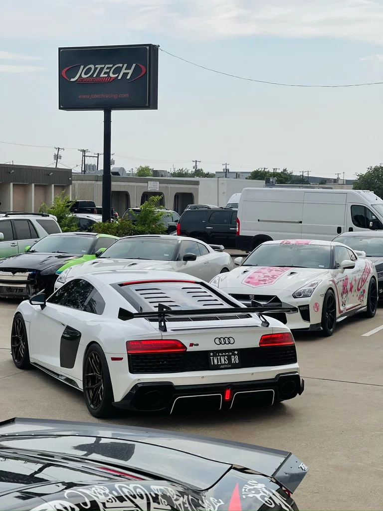An Audi R8 with a large rear wing and a Nissan GT-R with custom livery parked outside Jotech Motorsports performance shop.