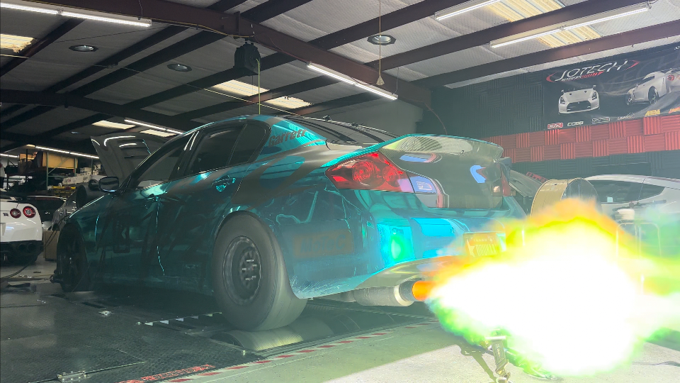 Infiniti G35 sedan on a dyno with vibrant flames shooting from the exhaust during a performance tuning session at Jotech Motorsports.