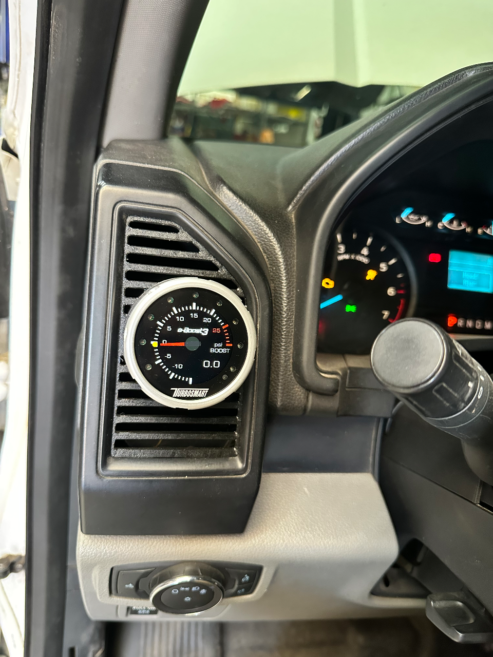 A Turbosmart boost gauge installed in the dashboard vent of a vehicle, showing 0.0 psi.