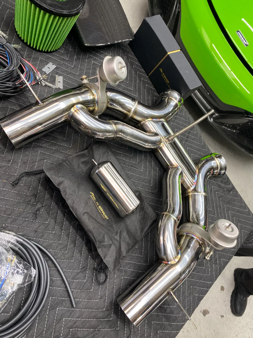 New FI Exhaust system and green air filter laid out on a shop blanket, with a bright green McLaren in the background, ready for installation.
