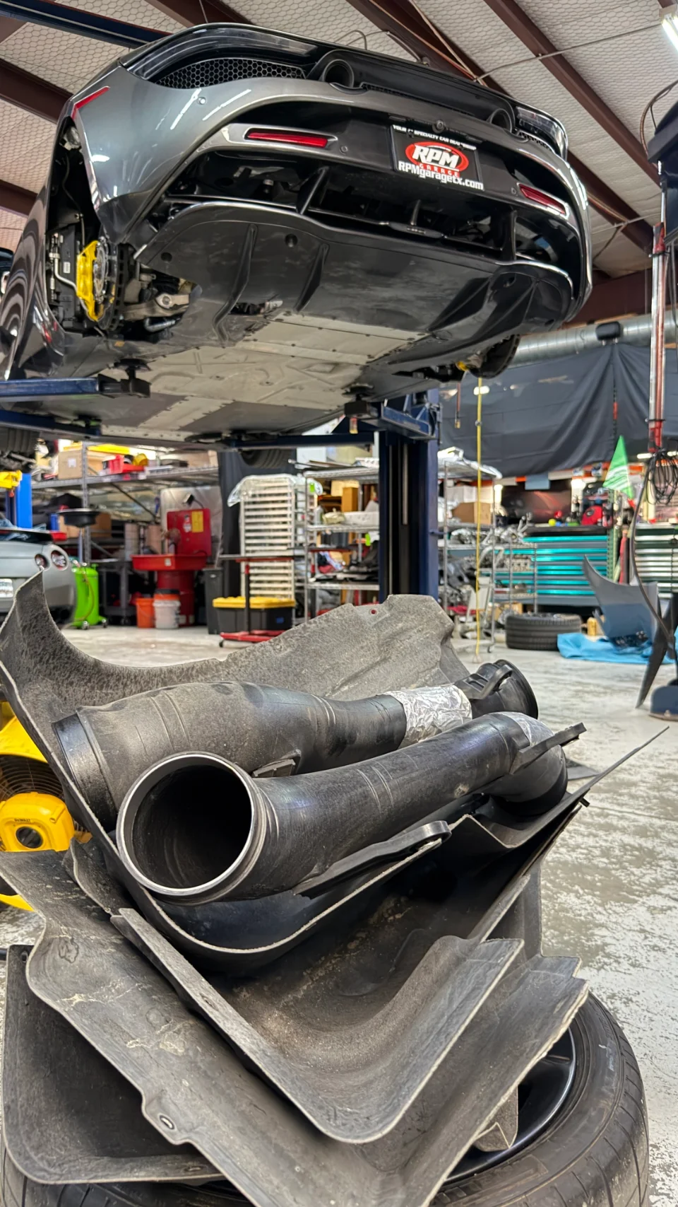 Rear underside of a grey McLaren on a lift in a performance shop, with removed boost pipes and underbody panels in the foreground.