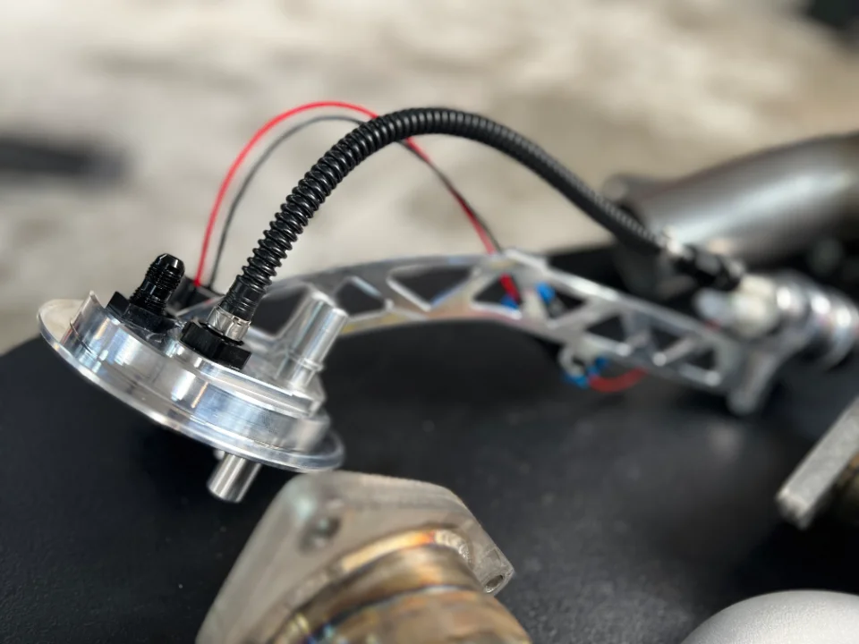 Close-up of an aftermarket fuel pump hanger assembly with AN fittings and braided lines.