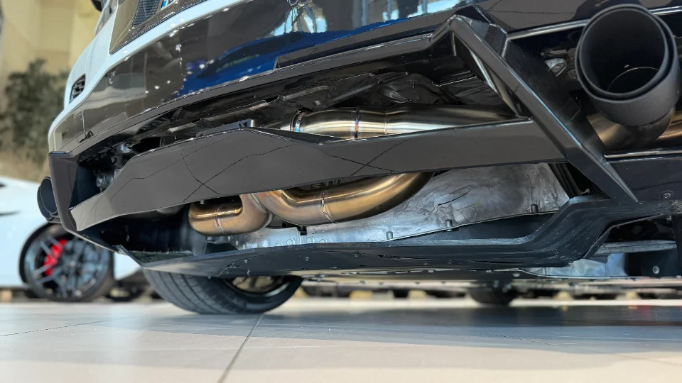 Detailed view of a performance exhaust system and rear diffuser on a white Corvette C8, showcasing the polished pipes.