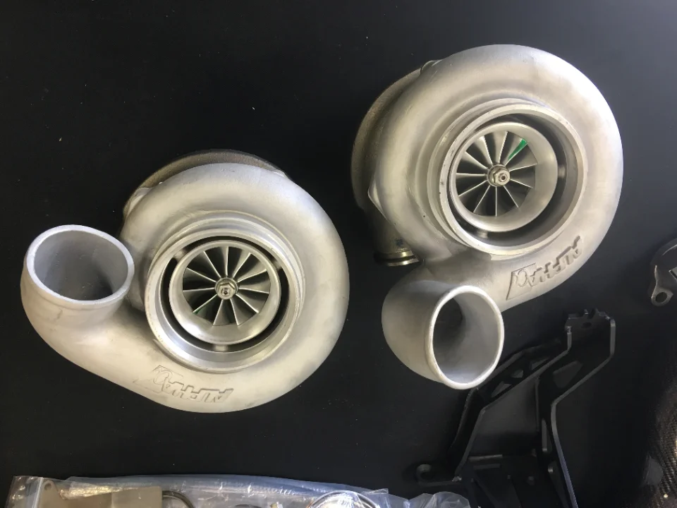 Two Alpha Performance turbochargers on a dark background, showcasing their compressor housings and impellers.