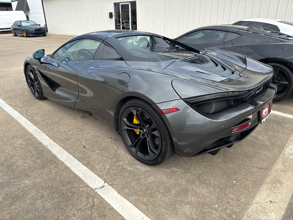 A sleek grey McLaren 720S supercar with yellow brake calipers parked in a lot outside a building.