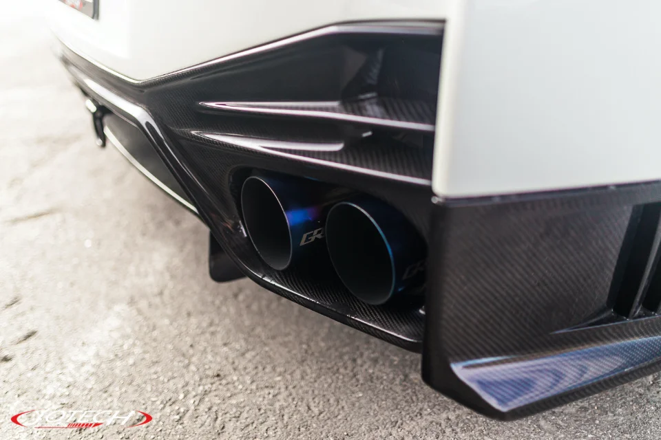 A close-up of a white Nissan GT-R's rear bumper featuring blue titanium exhaust tips and a carbon fiber diffuser.