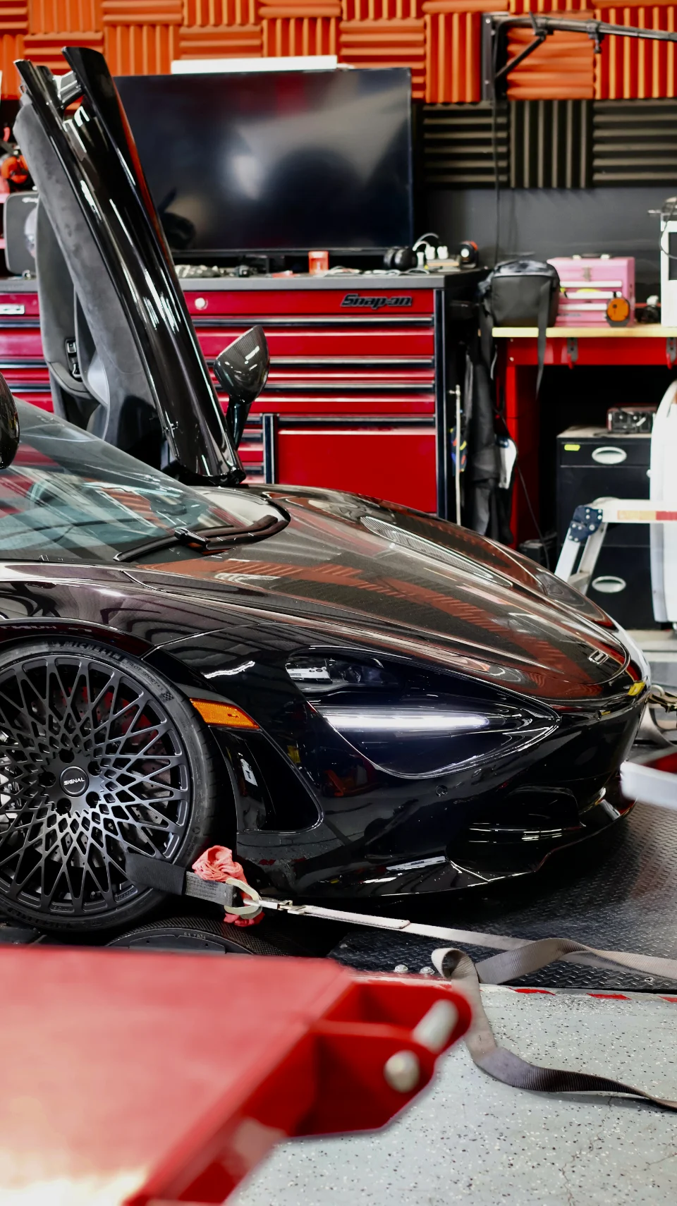 Black McLaren 720S strapped to a dynamometer for performance testing at a tuning shop.