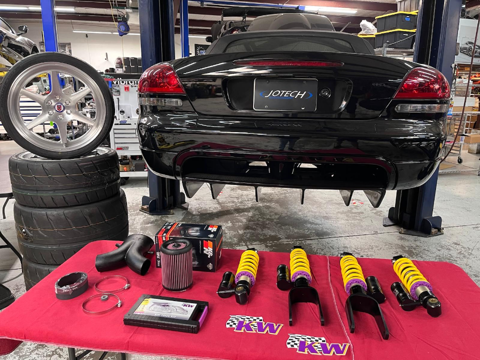 A black Dodge Viper on a lift in a Jotech Motorsports shop, with KW coilovers, K&N intake, and aftermarket wheels displayed.