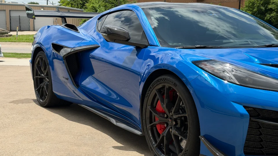 A blue Chevrolet Corvette C8 Z06 with a carbon fiber wing, black wheels, and red brake calipers parked outdoors.