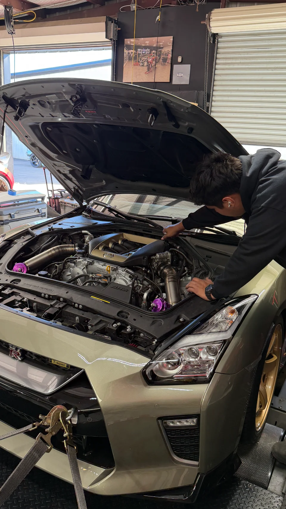 A person works on the engine bay of a gold Nissan GT-R R35 strapped to a dyno at Jotech Motorsports.