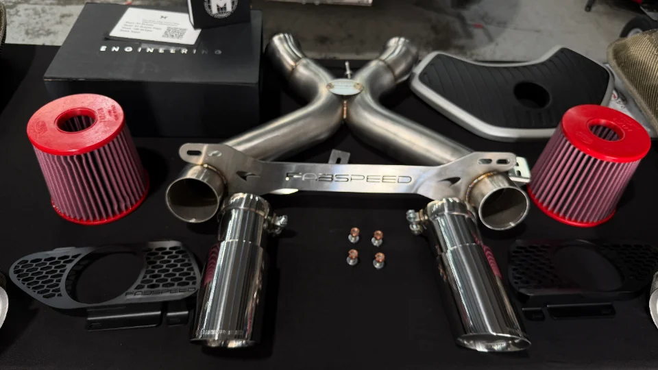 Fabspeed exhaust system with X-pipe, mufflers, and performance air filters displayed on a black surface.