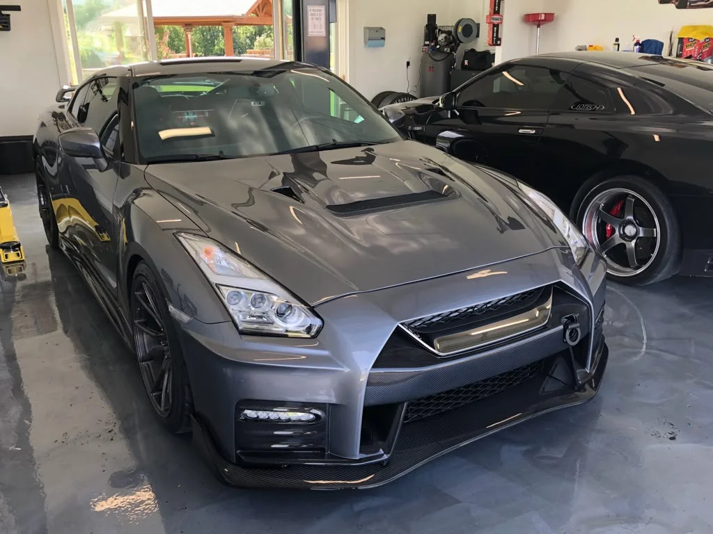 A grey Nissan GT-R with carbon fiber aero parked in a garage next to a black performance car.
