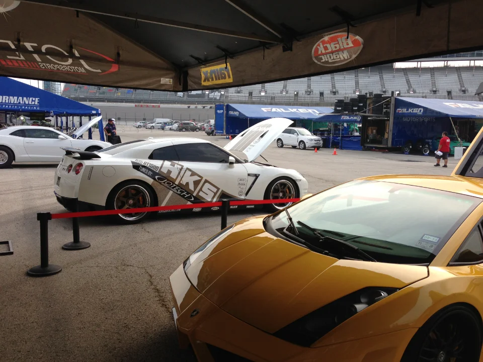 Nissan GT-R with Jotech livery, a yellow Lamborghini, and a white Chevrolet Camaro displayed under tents at a track event.
