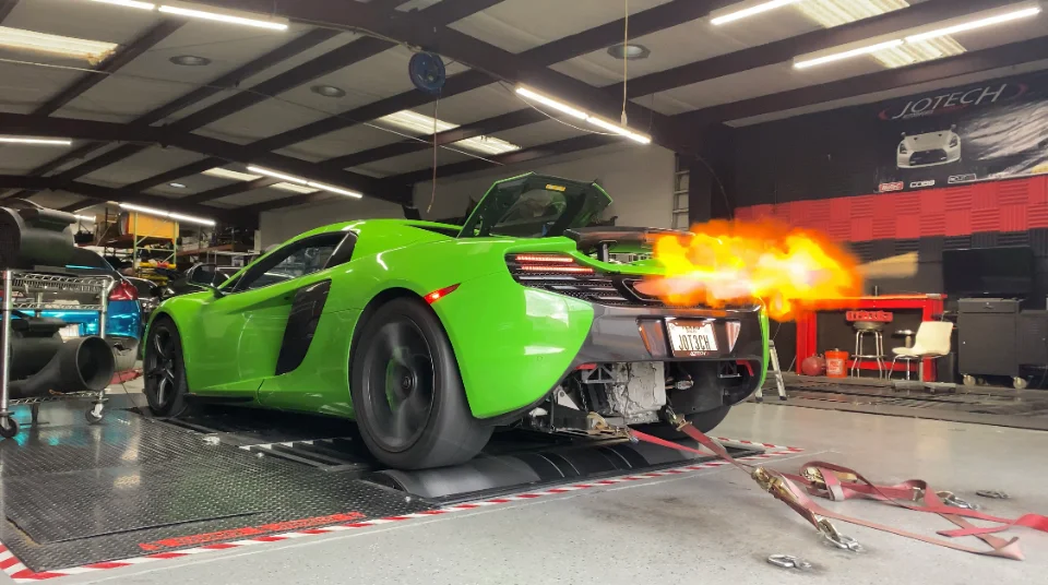 A vibrant green McLaren supercar on a dyno at Jotech Motorsports, shooting dramatic flames from its exhaust during a performance test.